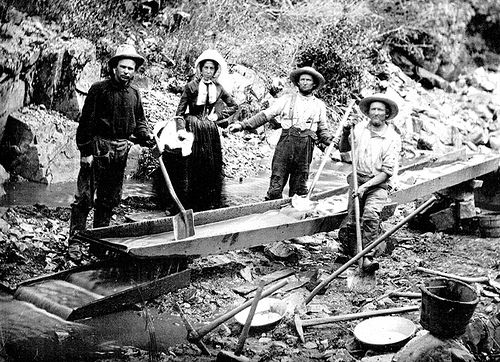 Three men and one woman panning for gold during the California Gold Rush